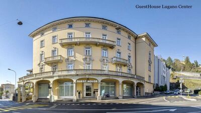 In Lugano (6900, Kanton Tessin) steht das elegante Gebaeude des GuestHouse Lugano Center mit seinen Rundbalkonen und klassischer Fassade an einer Strassenecke.