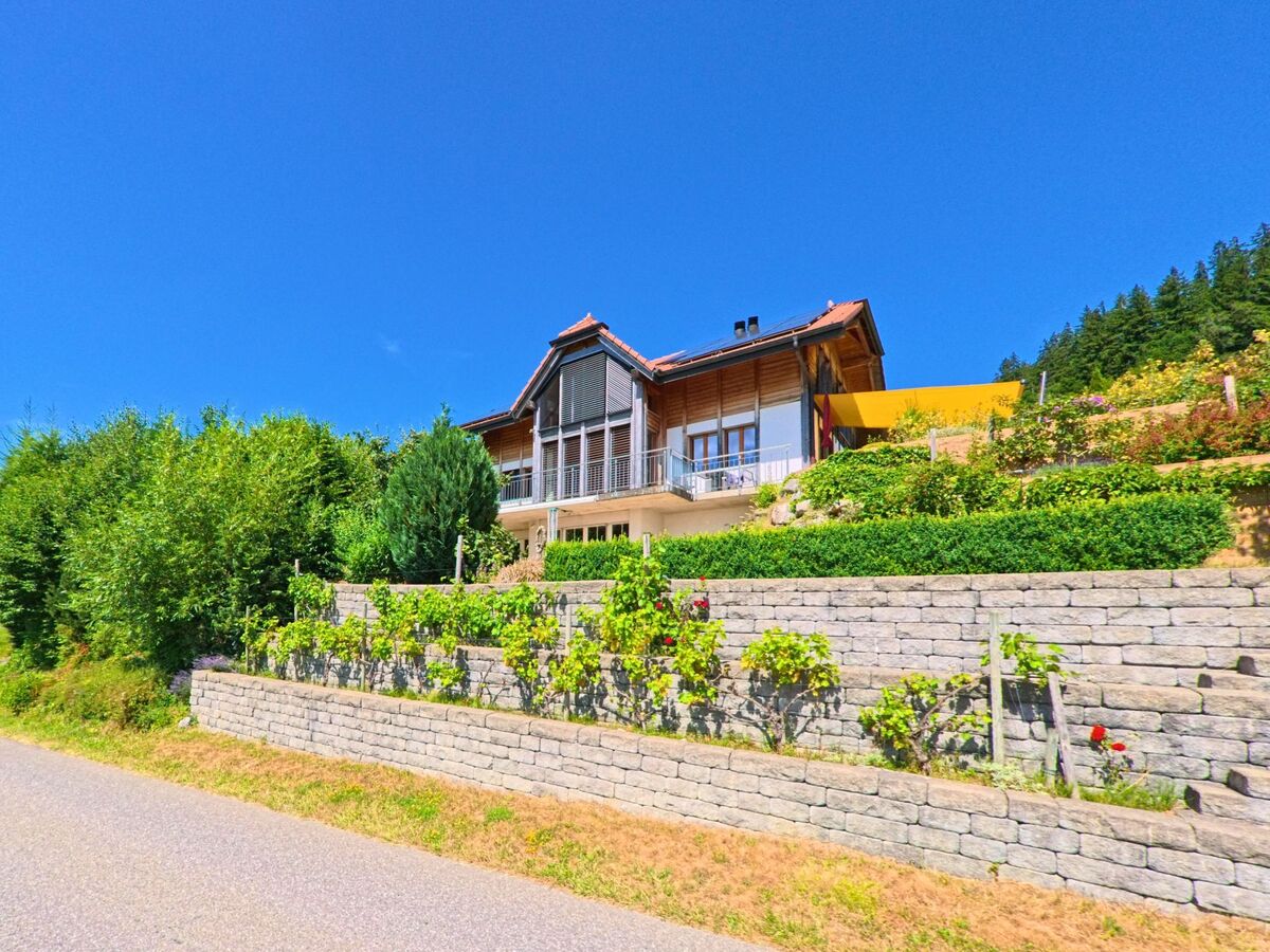 In Guggisberg (3158, Kanton Bern) steht ein modernes Haus mit grossen Glasfronten an einem Hang, umgeben von terrassierten Gartenanlagen und dichter Vegetation.