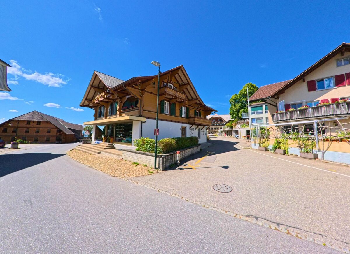 Im Zentrum von Guggisberg (3158, Kanton Bern) stehen traditionelle Häuser mit charakteristischen Holzbalkonen entlang einer leicht ansteigenden Strasse.