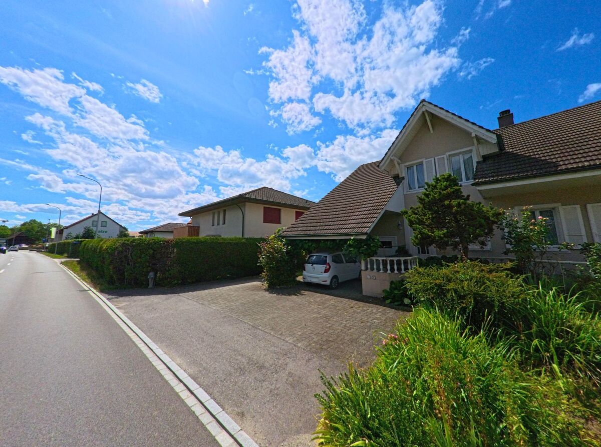 Ein Einfamilienhaus mit gepflegtem Vorgarten und Carport steht in Gunzgen (4617, Kanton Solothurn) an einer ruhigen Wohnstrasse unter blauem Himmel mit lockeren Wolken.