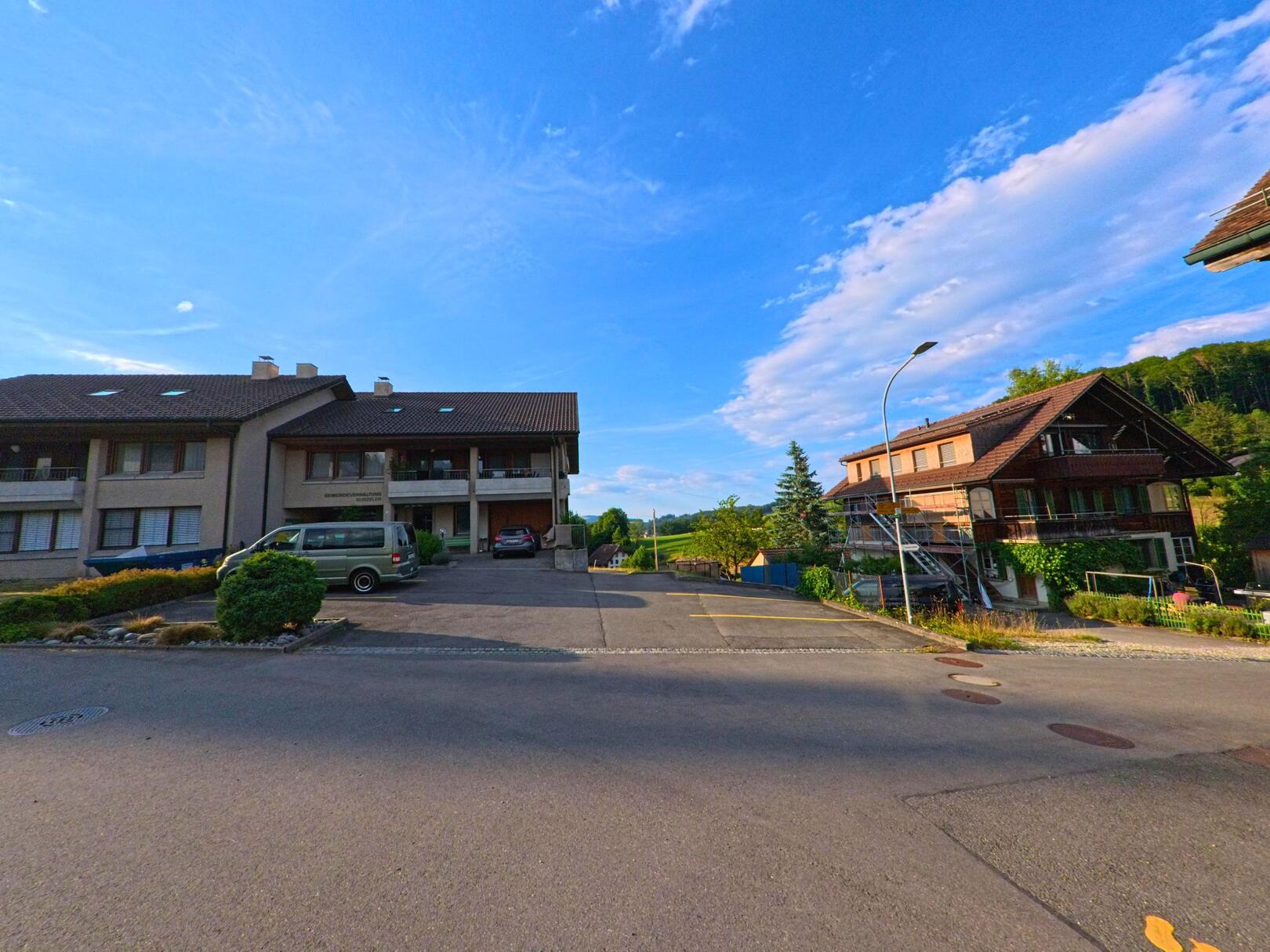 In Gurzelen (3663, Kanton Bern) treffen moderne Mehrfamilienhäuser und traditionelle Holzbauten in einer ruhigen Wohnstrasse aufeinander.