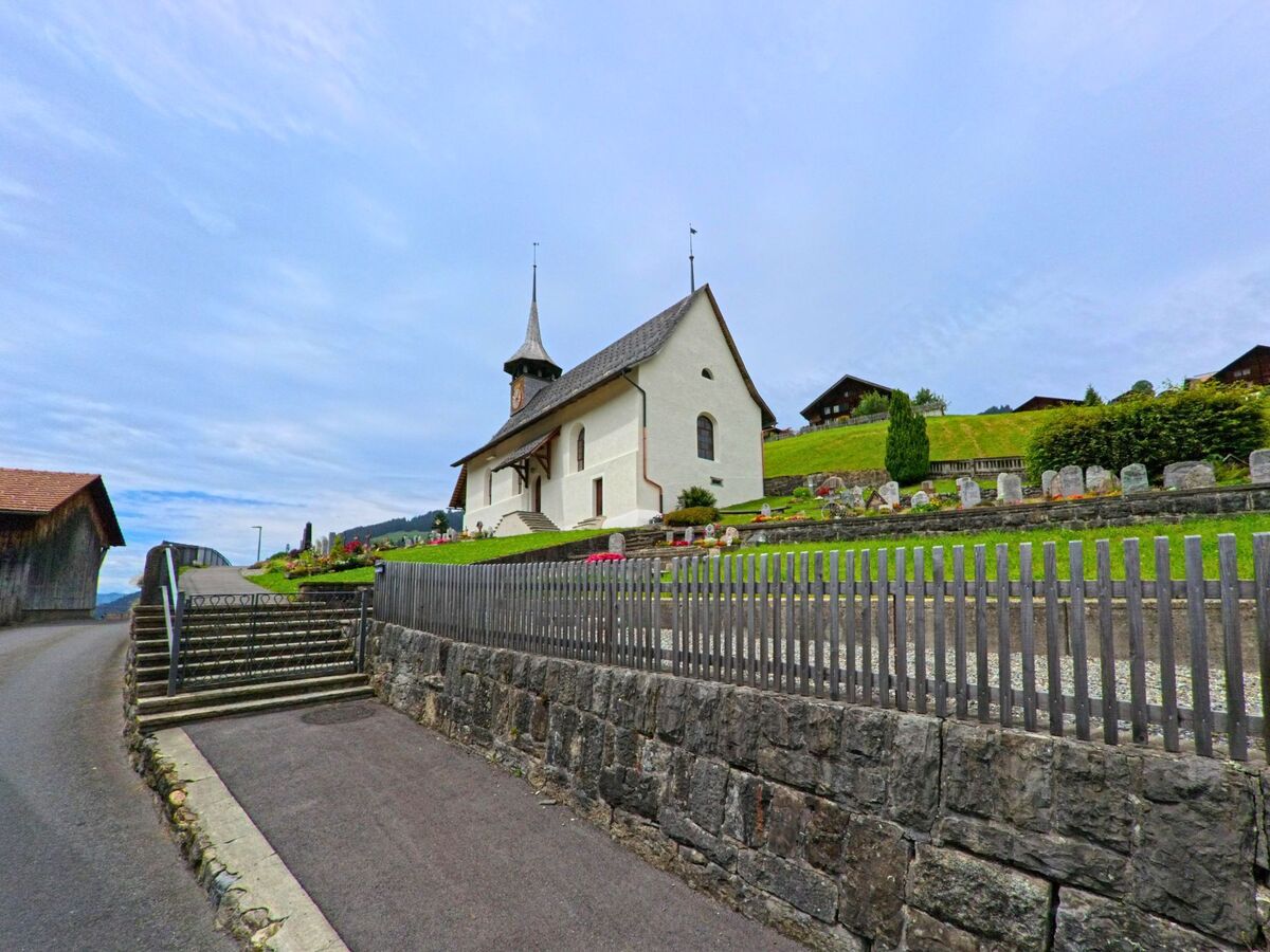 Auf einem Huegel in Habkern (3804, Kanton Bern) steht eine weisse Kirche mit spitzem Turm, umgeben von einem gepflegten Friedhof mit Grabsteinen.