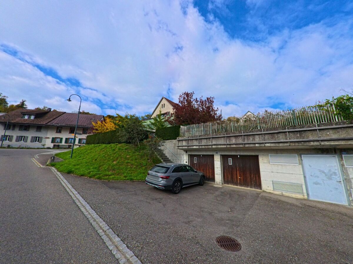 Am Hang einer Strasse in Habsburg (5245, Kanton Aargau) liegen Garagen mit Holzfronten unterhalb von Wohnhäusern und begrünten Gärten.