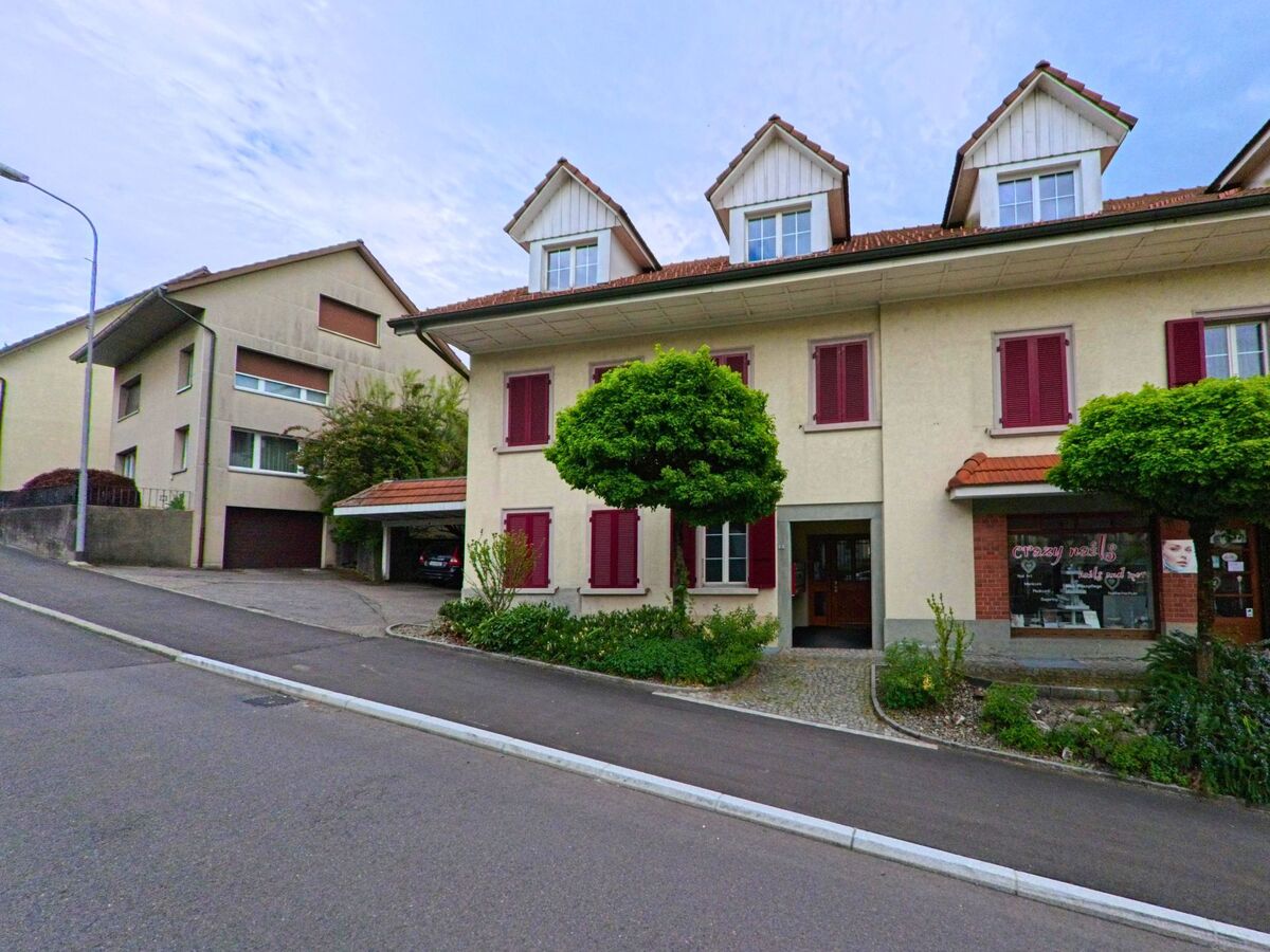 In Hägendorf (PLZ 4614, Kanton Solothurn) steht ein Wohn- und Geschaeftshaus mit roten Fensterlaeden und kleinen Läden an einer leicht ansteigenden Strasse.