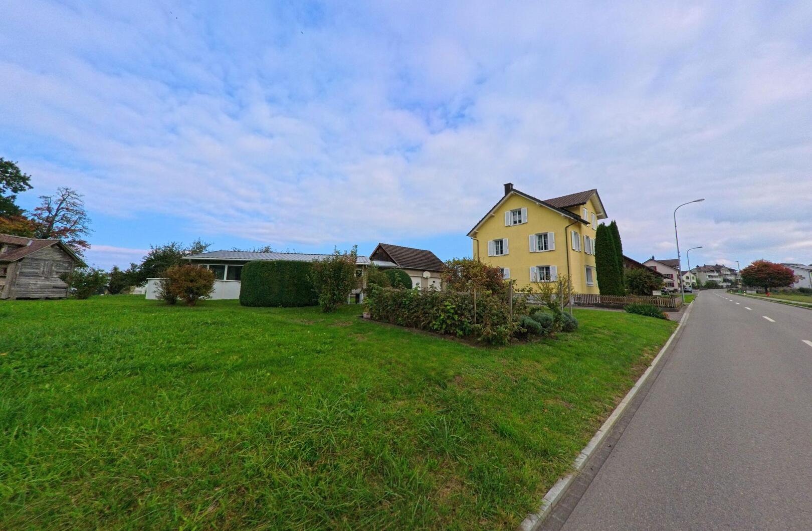 Ein gelbes Wohnhaus steht in Haeggenschwil (9308, Kanton St. Gallen) an einer ruhigen Strasse, umgeben von gepflegtem Garten und weiten Gruenflaechen.