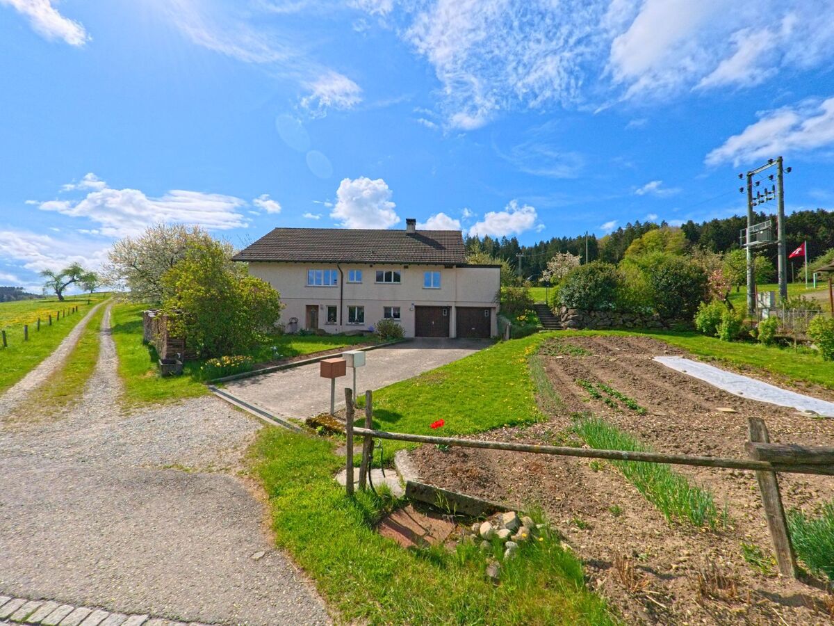 Ein Wohnhaus mit angrenzendem Gemüsegarten liegt in der Gemeinde Hagenbuch mit der PLZ 8523 im Kanton Zürich am Rand eines Wiesenwegs, der in die offene Landschaft führt.