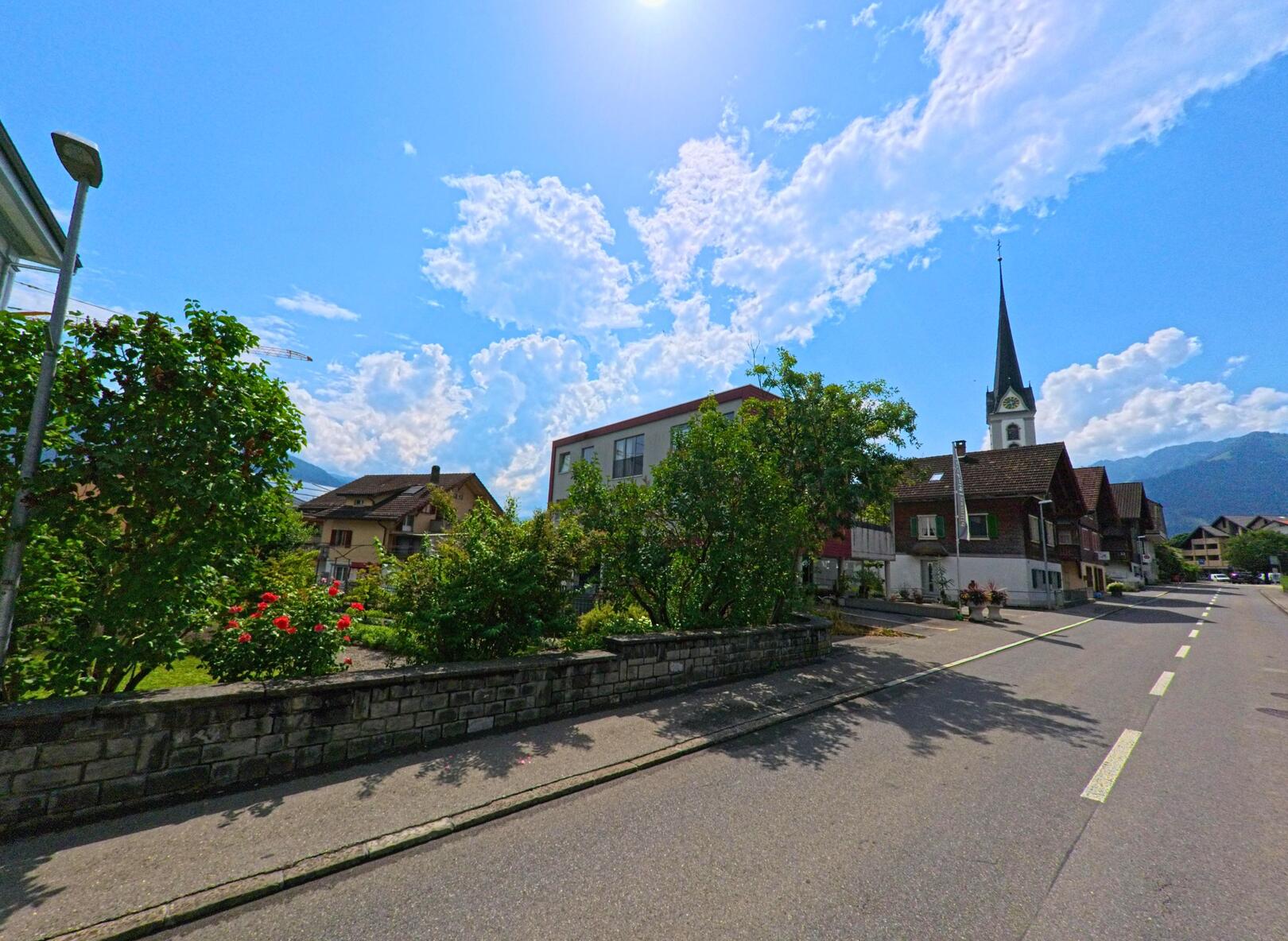 Die Kirche von Halten (6064, Kanton Solothurn) mit hohem Turm erhebt sich ueber Wohnhaeuser entlang einer ruhigen Strasse.