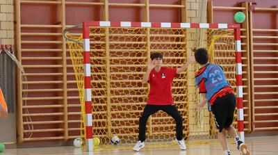 In Dietikon (8953, Kanton Zuerich) steht ein junger Torhueter konzentriert im Handballtor, waehrend ein Spieler im Angriff zum Wurf ansetzt.