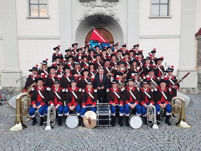 Die Harmonie-Musik Marbach posiert in Escholzmatt-Marbach (6196, Kanton Luzern) in historischen Uniformen mit Blas- und Schlaginstrumenten vor einer Kirche.