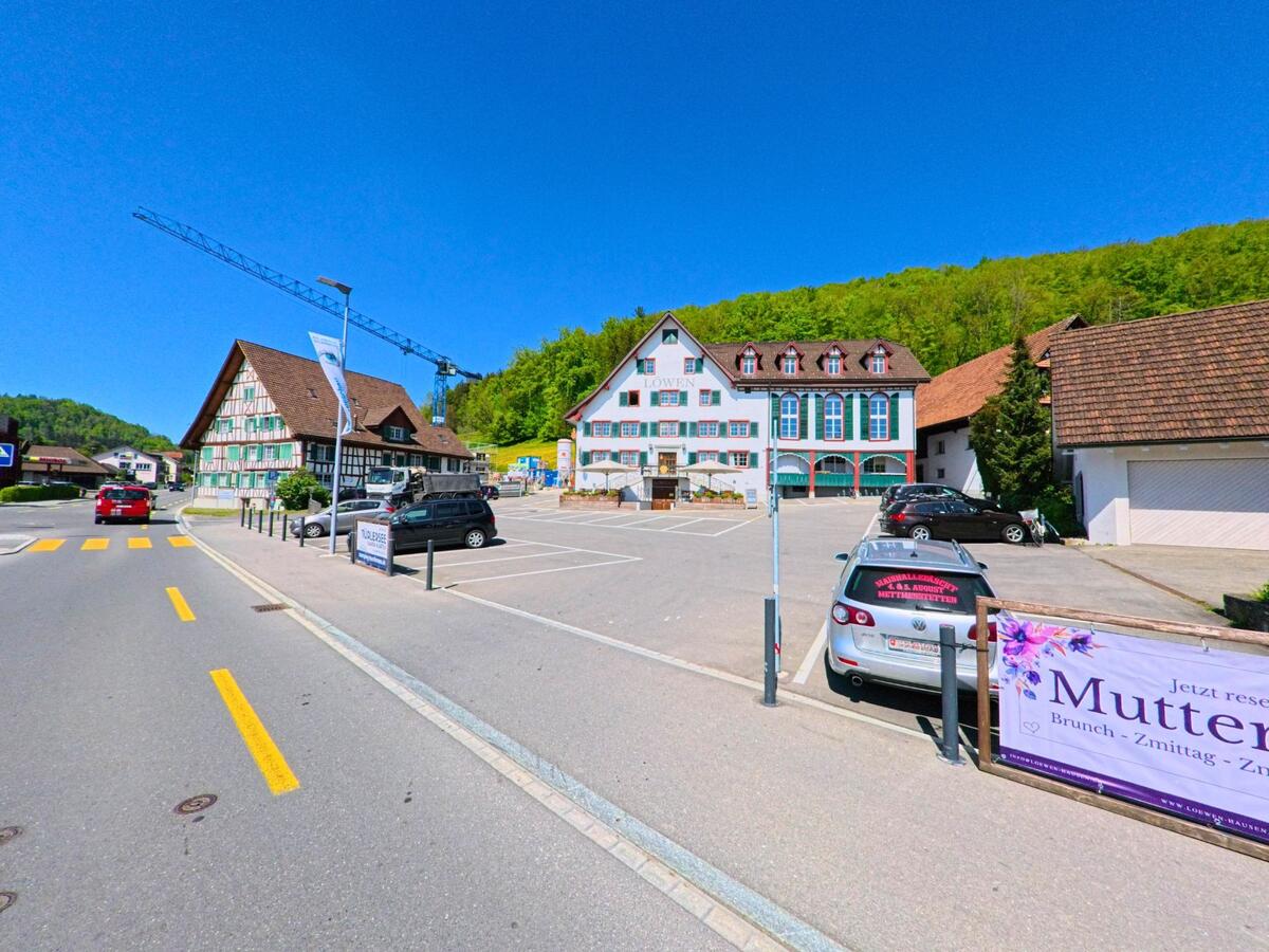  Im Ortskern von Hausen am Albis (8915, Kanton Zürich) liegen ein traditionsreiches Gasthaus mit Fachwerkfassade und ein grosser Parkplatz vor einem Waldrand.