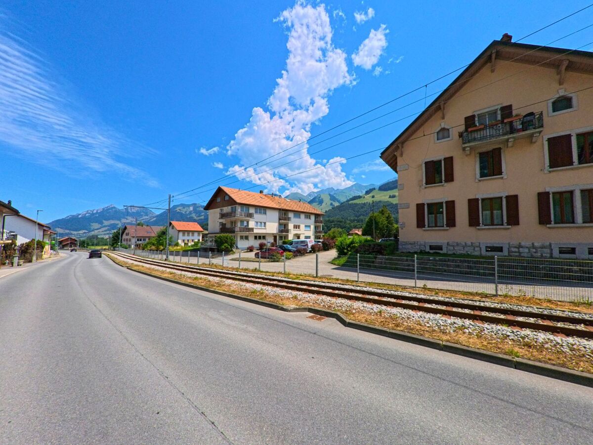 An der Durchgangsstrasse von Haut-Intyamon (1669, Kanton Freiburg) reihen sich Wohnhäuser mit roten Ziegeldächern entlang der Bahnlinie vor der Kulisse der Freiburger Voralpen.