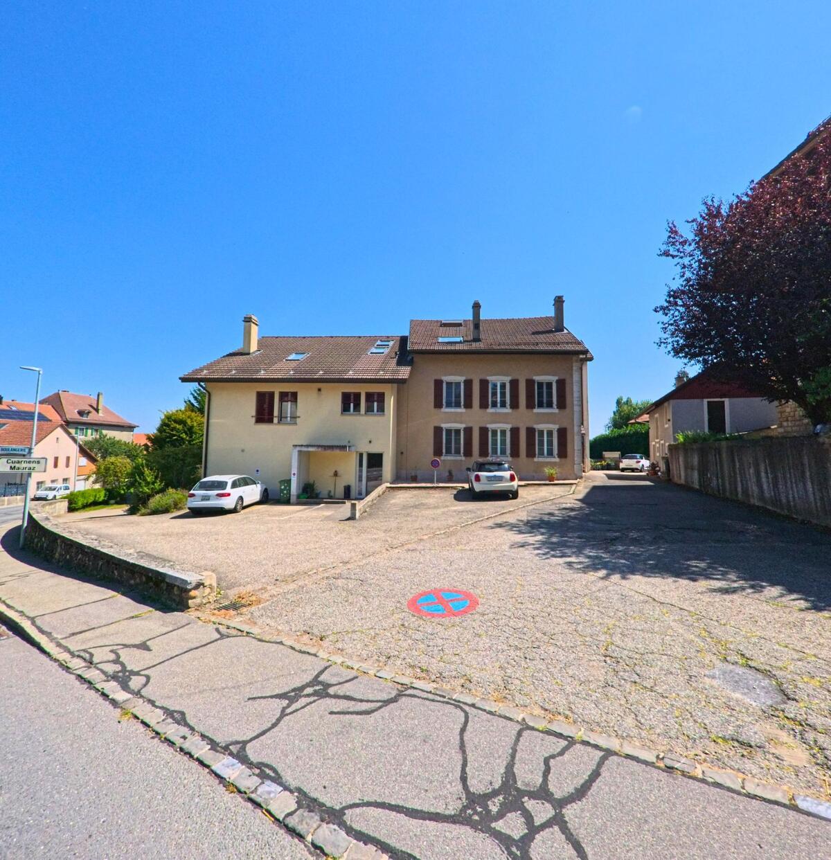 Ein Wohnhaus mit braunen Fensterlaeden und vorgelagertem Parkplatz praegt das Strassenbild in Hautemorges (1142, Kanton Waadt).