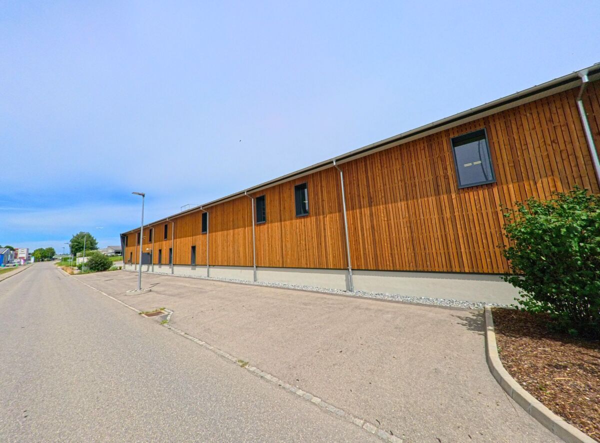 In Hauterive (1730, Kanton Freiburg) verläuft eine ruhige Strasse entlang eines modernen Holzgebäudes mit schlichten Fenstern und klaren Linien.