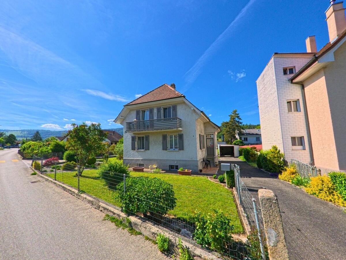 In Haute-Sorne (2854, Kanton Jura) steht ein gepflegtes Einfamilienhaus mit Balkon und Vorgarten zwischen weiteren Wohnhäusern in einer ruhigen Quartierstrasse.