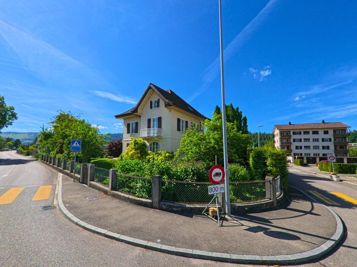 In Haute-Sorne (2854, Kanton Jura) steht ein freistehendes Wohnhaus mit markantem Giebeldach an einer Strassengabelung mit Fussgängerstreifen und Verkehrsschildern.