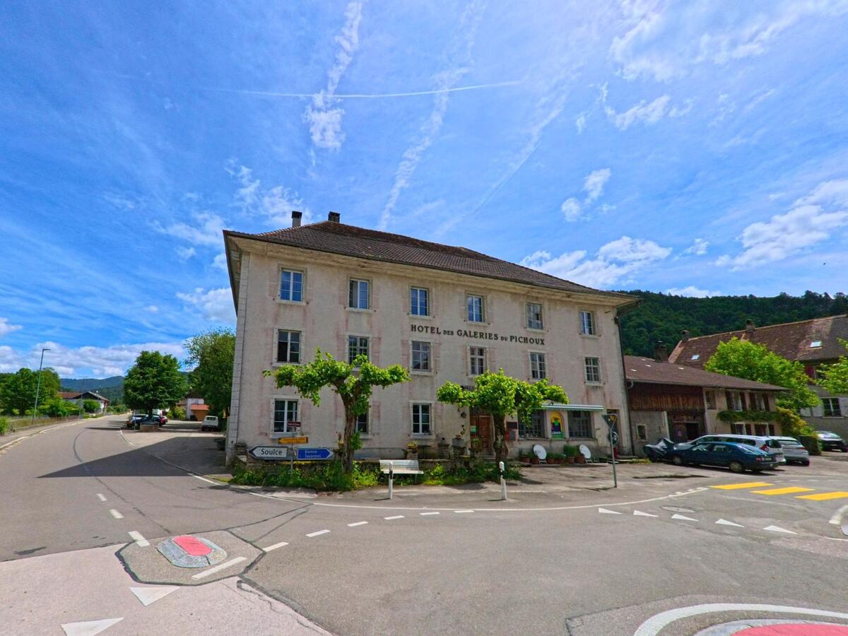 In Haute-Sorne (2863, Kanton Jura) steht das historische Gebäude des Hôtel des Galeries du Pichoux an einer markanten Weggabelung mit Verkehrsschildern und Fussgängerstreifen.