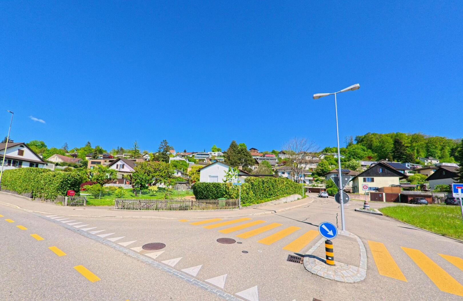 In Hedingen (8908, Kanton Zürich) führt eine schmale Strasse vorbei an Einfamilienhäusern und gepflegten Gärten, während sich das Wohngebiet sanft den Hügel hinaufzieht.