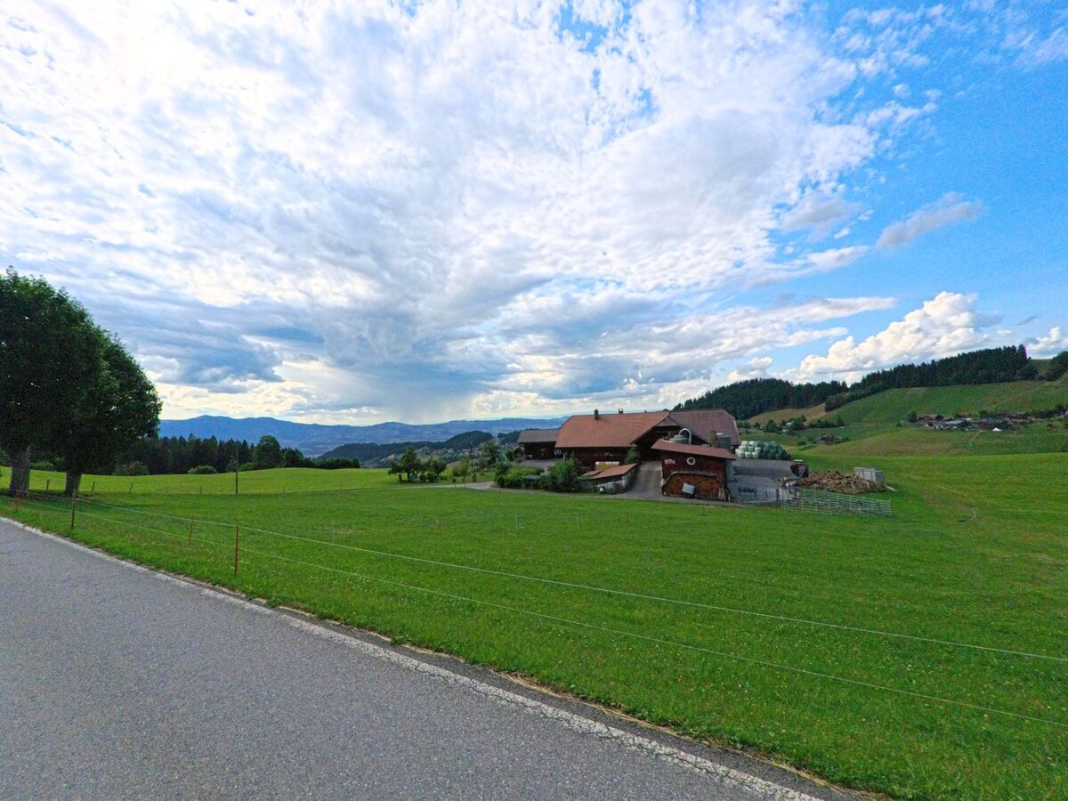 Inmitten der offenen Landschaft von Heiligenschwendi (3625, Kanton Bern) liegt ein grosser Bauernhof mit Wirtschaftsgebaeuden und weitem Blick in ein sanftes Tal.