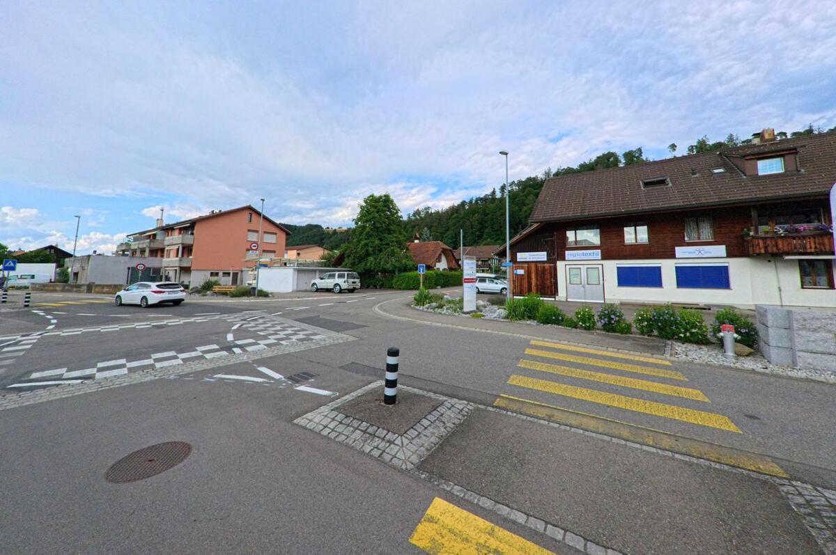 In Heimberg (3627, Kanton Bern) treffen sich mehrere Strassen an einem kleinen Verkehrsknotenpunkt mit Zebrastreifen und gemischter Wohn- und Geschäftsbebauung.
