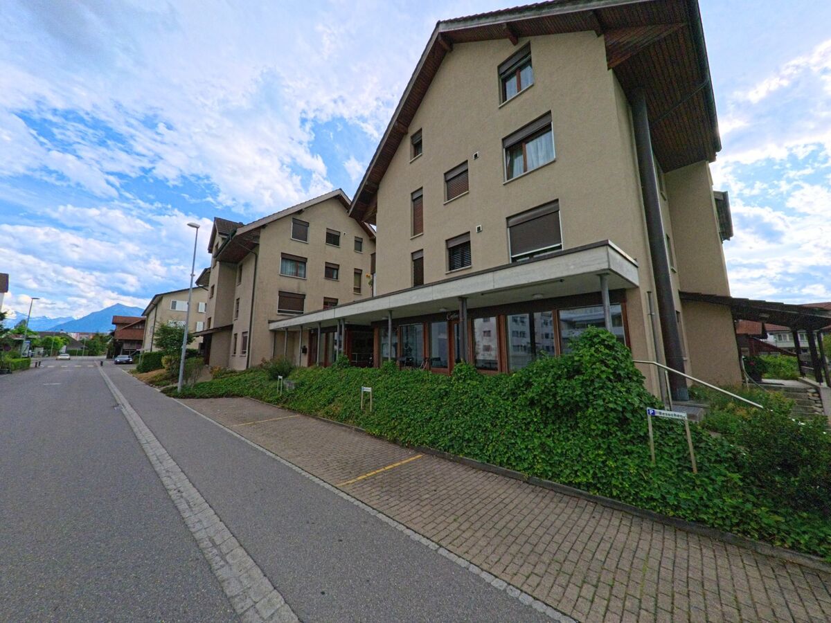 In Heimberg (3627, Kanton Bern) erstrecken sich mehrstöckige Wohnhäuser mit begrünten Eingangsbereichen entlang einer ruhigen Quartierstrasse mit Blick auf die Voralpen.
