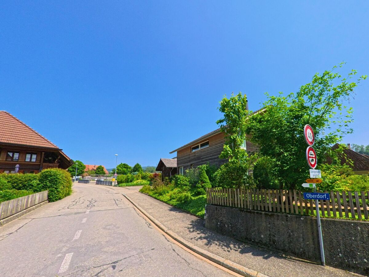 In der Oberdorfstrasse von Heimiswil (3412 im Kanton Bern) säumen gepflegte Holzhäuser eine verkehrsberuhigte Zone bei sommerlichem Wetter.