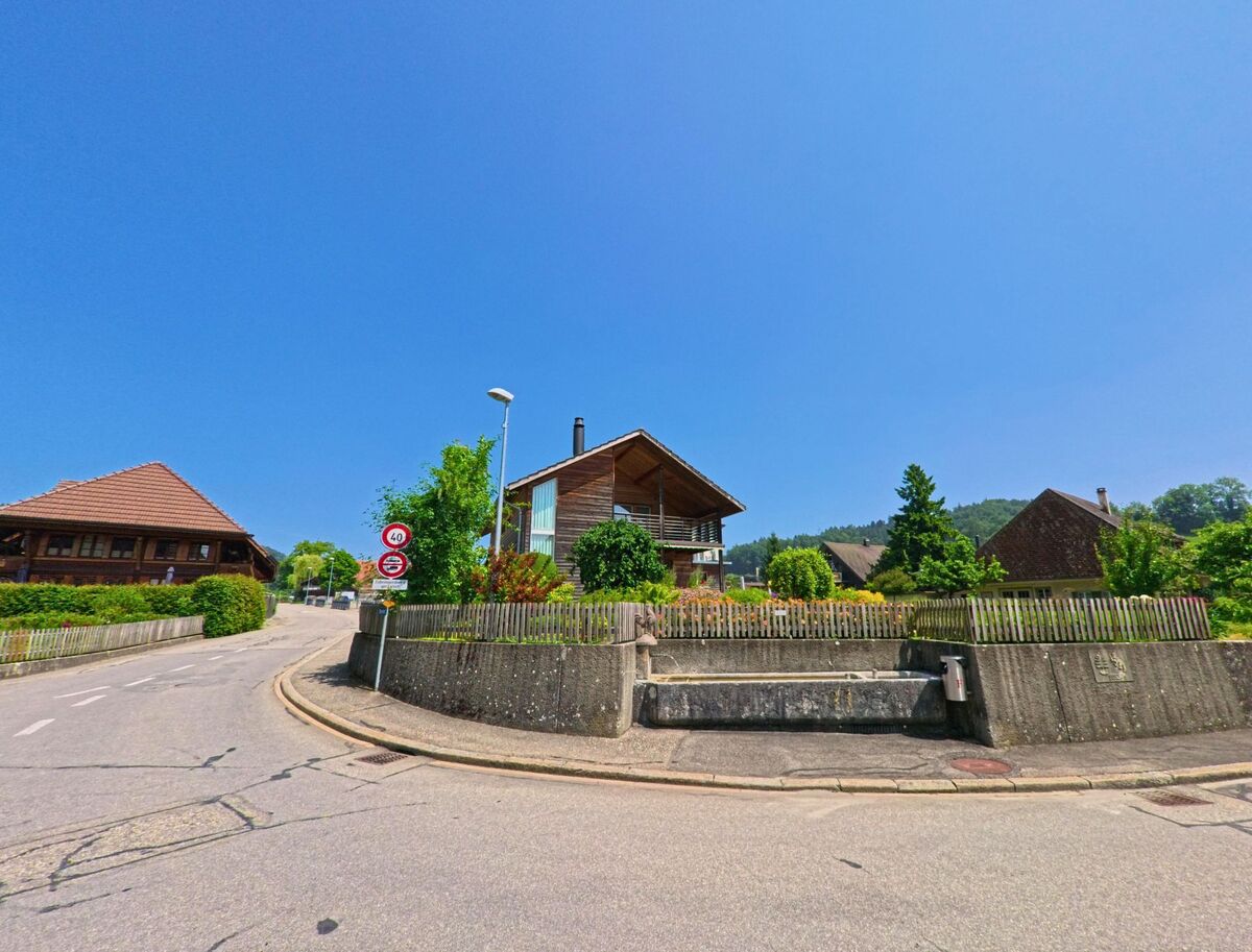 In einem ruhigen Wohnquartier von Heimiswil (3412, Kanton Bern) säumen moderne und traditionelle Einfamilienhäuser eine leicht ansteigende Strasse unter strahlend blauem Himmel.
