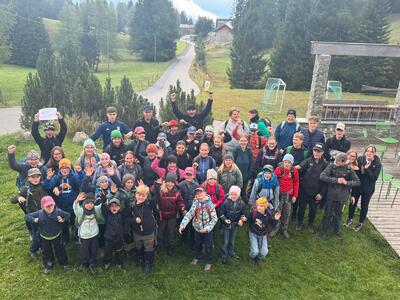 Die Teilnehmenden des Hela Niederbuchsiten aus Niederbuchsiten (4626, Kanton Solothurn) posieren gemeinsam mit Rucksäcken und Outdoor-Kleidung auf einer Wiese in einer ländlichen Berglandschaft.