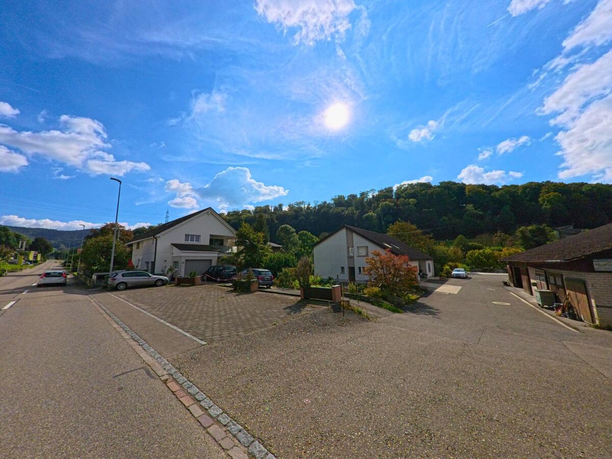 Unter blauem Himmel liegen in Hellikon (4316, Kanton Aargau) moderne Einfamilienhaeuser mit gepflegten Vorplaetzen am Rand eines bewaldeten Huegels.