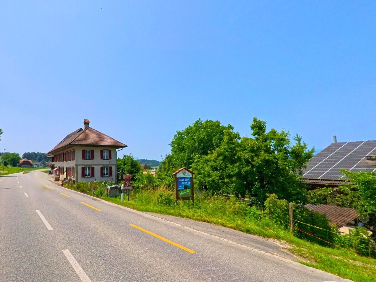An der Hauptstrasse von Hellsau (3429, Kanton Bern) stehen ein Wohnhaus mit roten Fensterläden und ein landwirtschaftliches Gebäude mit Solarpanelen.