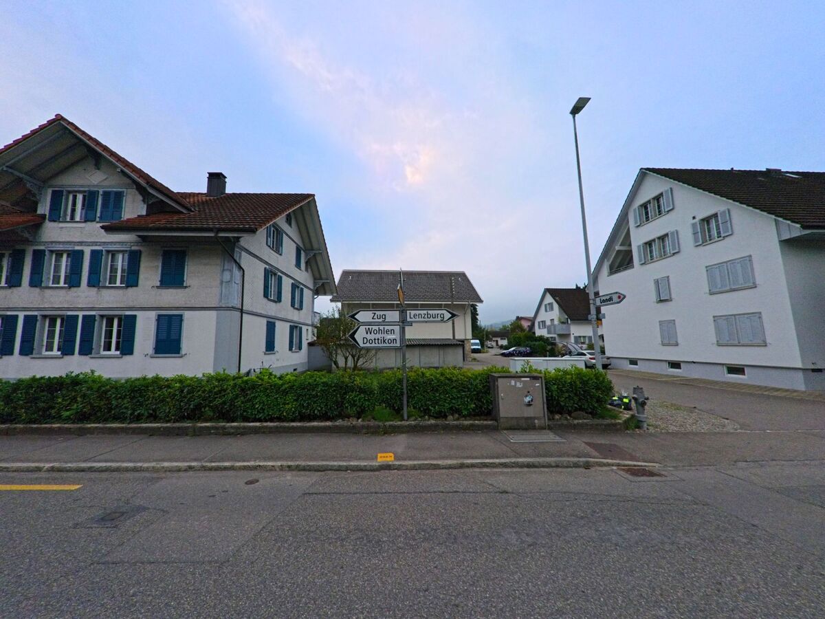 Ein Wegweiser mit Richtungen nach Lenzburg, Wohlen und Dottikon steht in Hendschiken (5604, Kanton Aargau) zwischen gepflegten Wohnhaeusern.