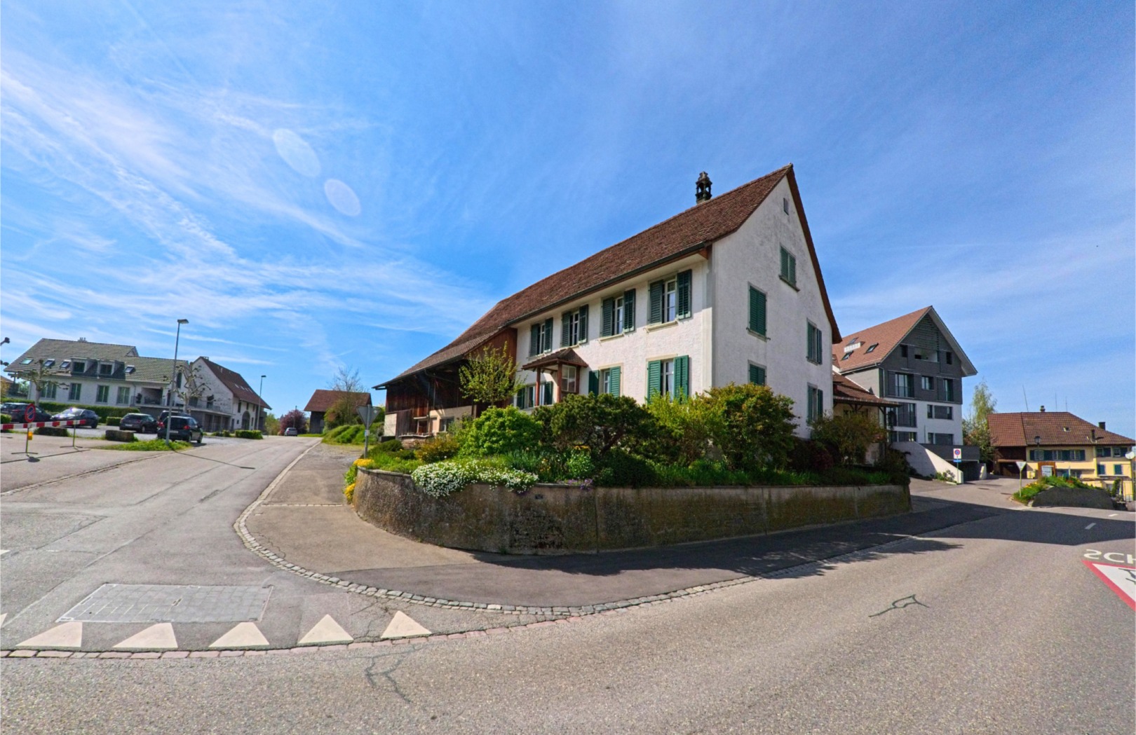 In der Gemeinde Henggart mit der PLZ 8444 im Kanton Zürich steht ein traditionelles Wohnhaus mit grün gestrichenen Fensterläden an einer ruhigen Kreuzung.