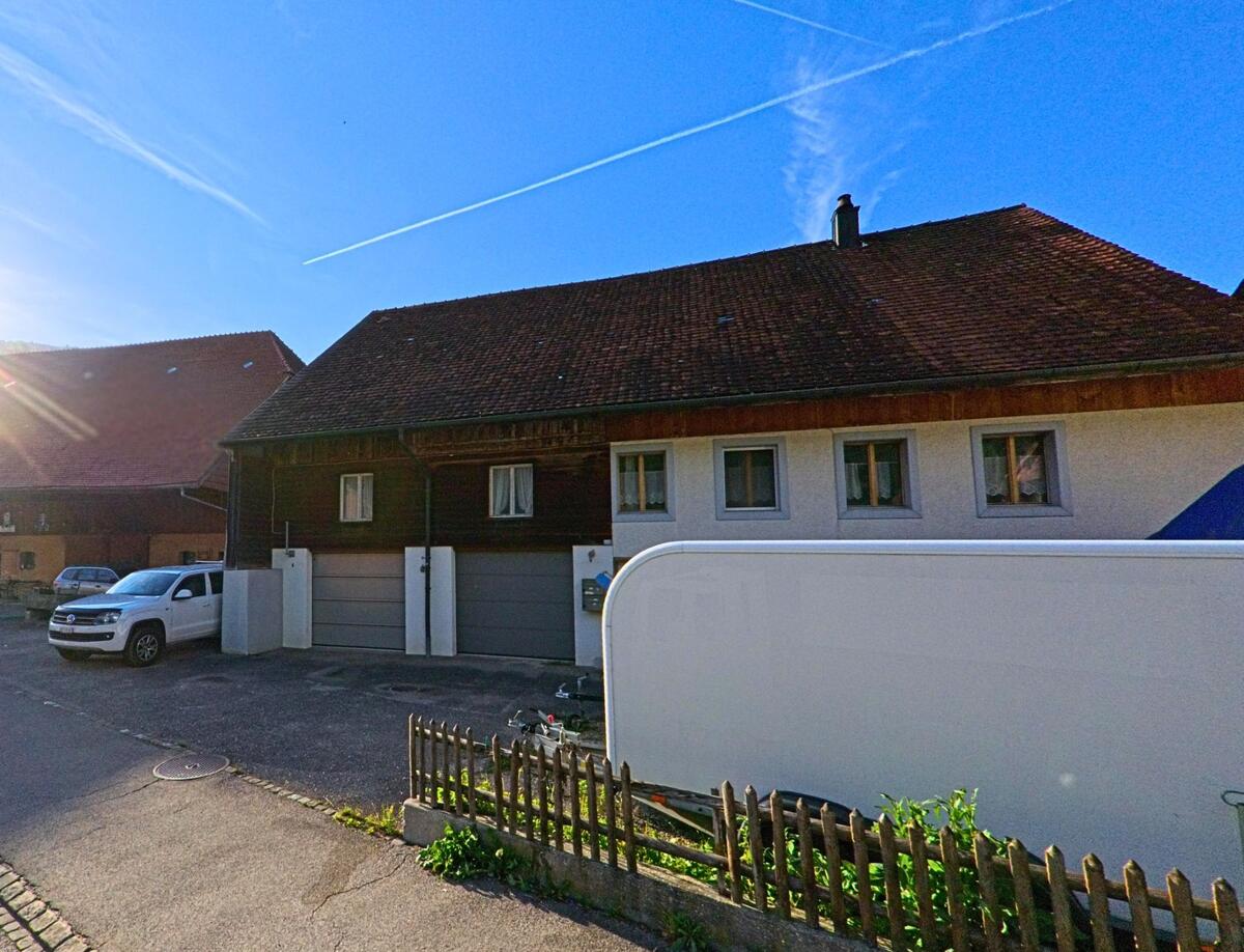 In Herbetswil (4715, Kanton Solothurn) steht ein Wohnhaus mit angebauter Garage und traditionellem Ziegeldach, davor sind ein Lieferwagen und ein Anhänger geparkt.