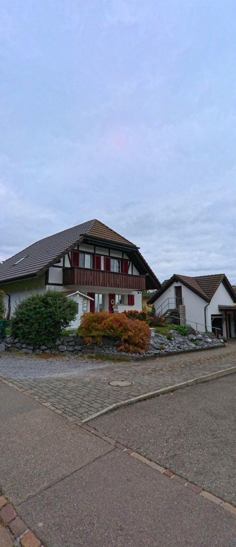 Mit Blick auf ein Haus mit Balkon und roten Fensterläden zeigt das Bild in Herdern (8535, Kanton Thurgau) einen gepflegten Vorgarten mit Steinen und Sträuchern.