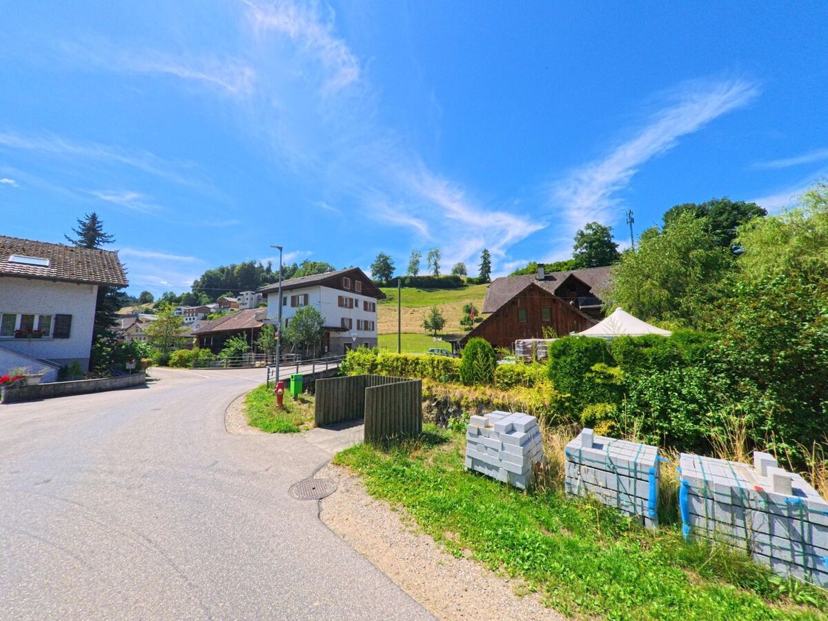 In Hergiswil bei Willisau (6133, Kanton Luzern) schlängelt sich eine schmale Strasse durch ein ruhiges Wohnquartier mit traditionellen Häusern und angrenzender Hügellandschaft.