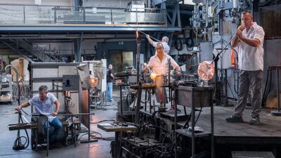 In der Werkhalle der Hergiswiler Glas AG in Hergiswil am See (6052, Kanton Nidwalden) formen Glasbläser glühende Glasobjekte an ihren Arbeitsplätzen vor den Öfen.