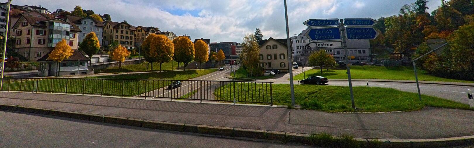 In Herisau (9100, Kanton Appenzell Ausserrhoden) zeigt das Bild eine Kreuzung mit Wegweisern, umgeben von herbstlichen Baumen und Wohnhaeusern am Hang.