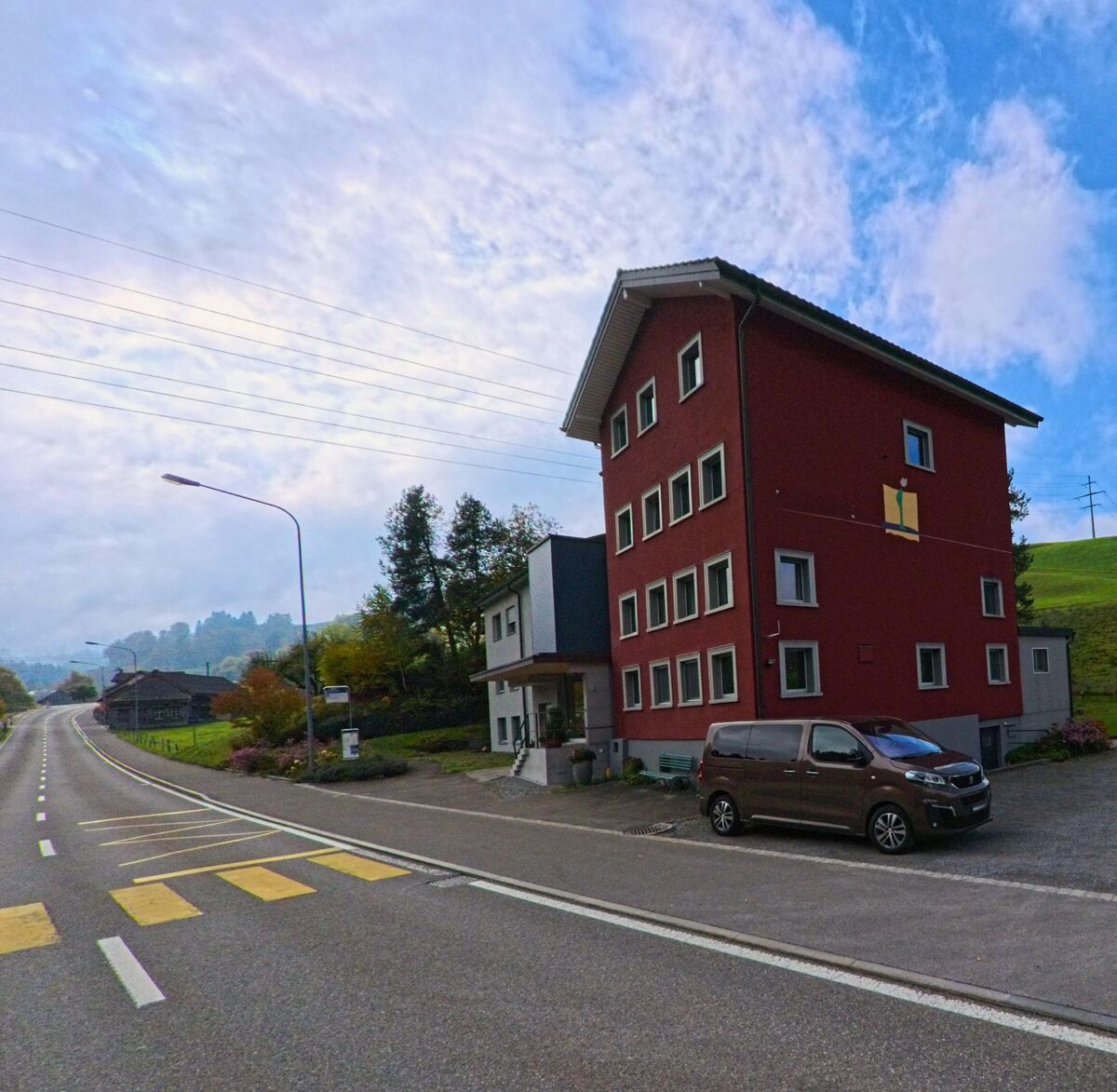 Ein rotes Mehrfamilienhaus prägt eine Kreuzung an der Durchgangsstrasse von Herisau (9100, Kanton Appenzell Ausserrhoden).