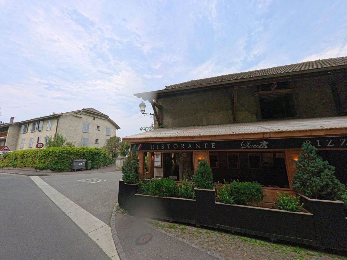 In Hermance (1248, Kanton Genf) befindet sich ein Ristorante mit vorgelagerter Terrasse und grünen Pflanzen entlang der Strasse.