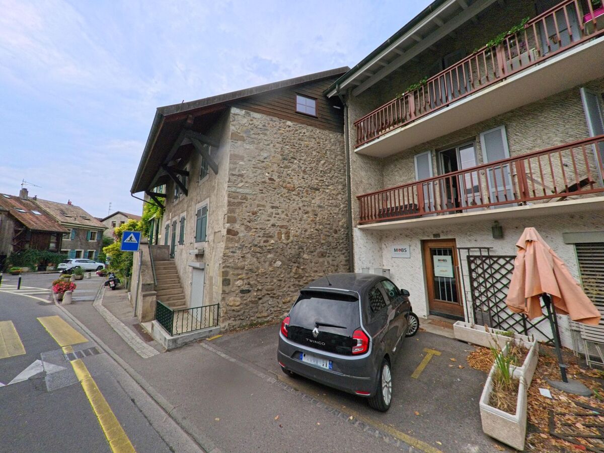 In Hermance (1248, Kanton Genf) stehen ein historisches Steinhaus mit Treppe und ein Wohnhaus mit Balkonen nebeneinander.