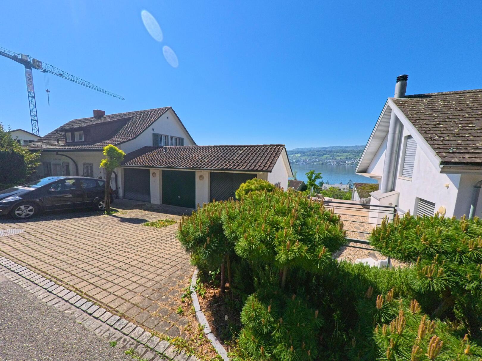 In Herrliberg, PLZ 8704 im Kanton Zürich, bietet eine Wohnstrasse mit Einfamilienhäusern einen weiten Blick über den Zürichsee und das gegenüberliegende Ufer.