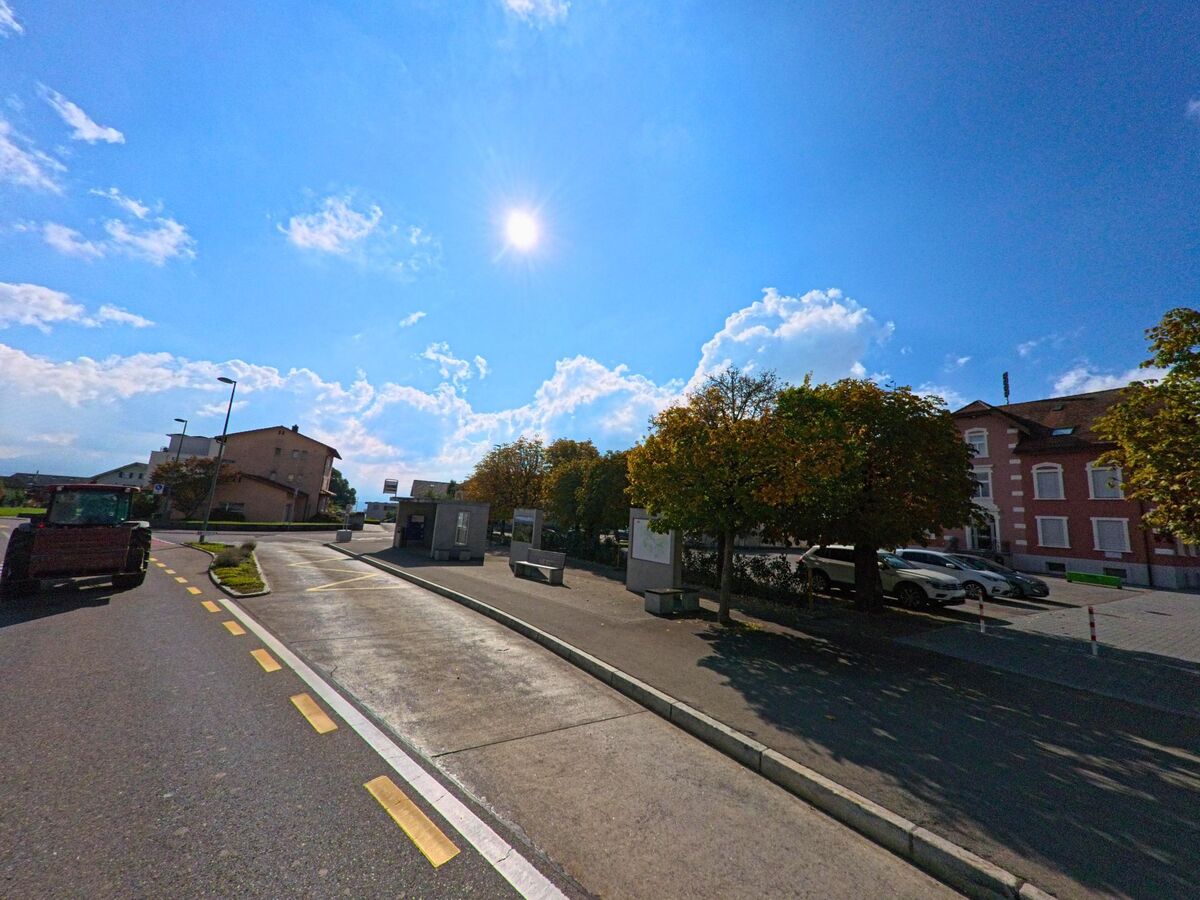 Mit Blick auf Bäume und Gebäude führt eine breite Fahrbahn durch Hildisrieden (6024, Kanton Luzern).