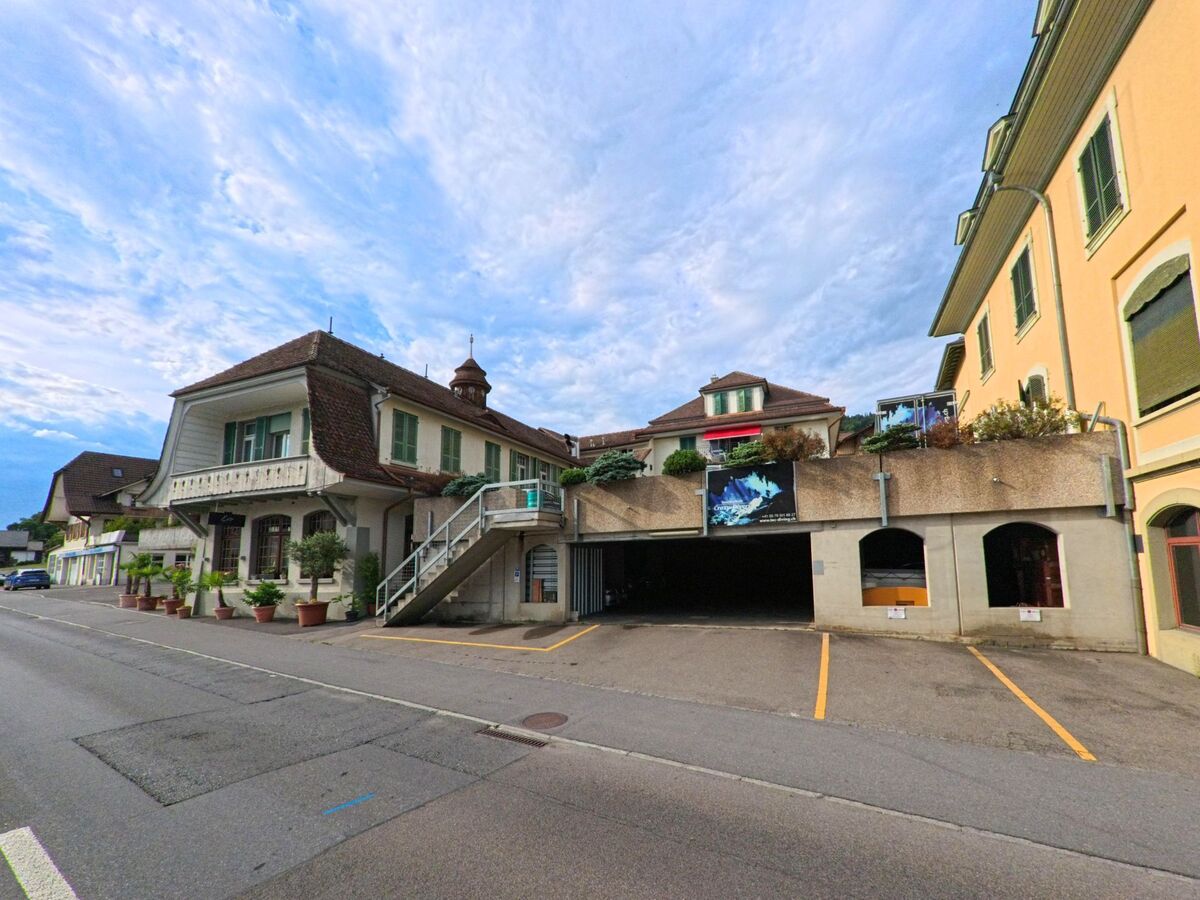 In Hilterfingen (3652, Kanton Bern) liegen historische Wohnhäuser mit Laubengängen und eine Garageneinfahrt nebeneinander entlang einer ruhig verlaufenden Strasse.