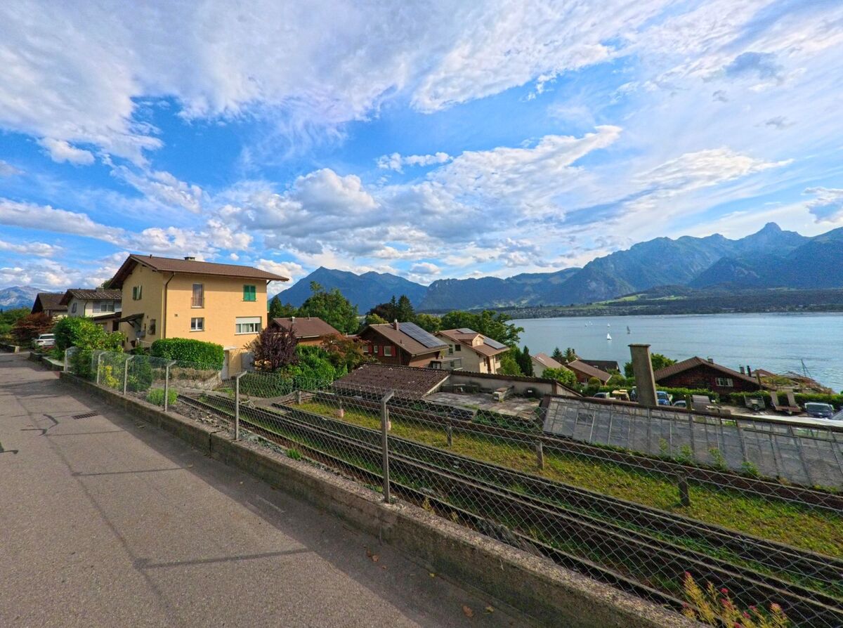 In Hilterfingen (3652, Kanton Bern) bietet eine Hangstrasse mit Wohnhäusern einen weiten Blick über den Thunersee und das umliegende Alpenpanorama.