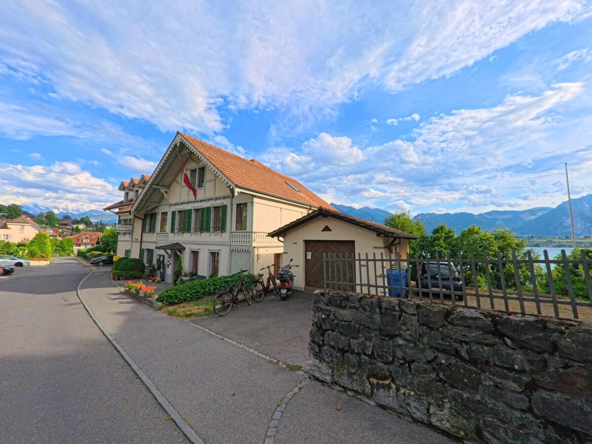 In Hilterfingen (3652, Kanton Bern) steht ein traditionelles Wohnhaus mit grünen Fensterläden oberhalb des Thunersees, umgeben von einer ruhigen Quartierstrasse.