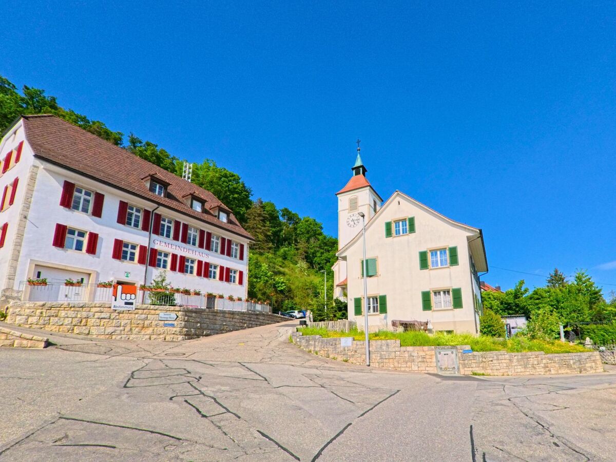 In Himmelried (4204 im Kanton Solothurn) stehen das Gemeindehaus mit roten Fensterläden und die Kirche mit Uhrturm markant nebeneinander am Hang.