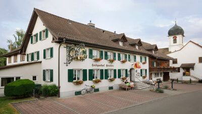 Der Landgasthof Hirschen in Ramsen (8262, Kanton Thurgau) ist ein traditionelles Gebäude mit grünen Fensterläden, Blumenschmuck und gemütlicher Sitzgelegenheit vor dem Haus.