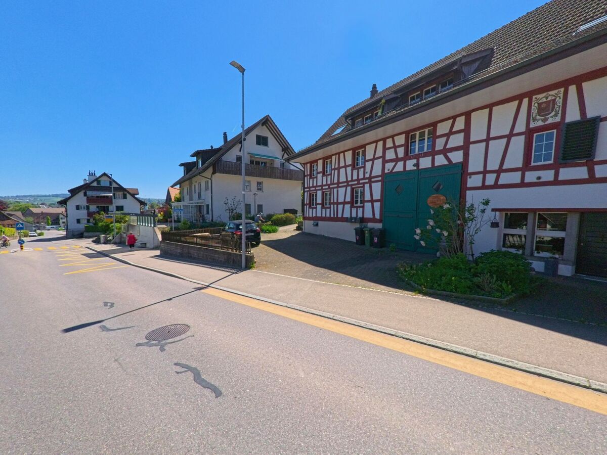 In Hochfelden (8182, Kanton Zürich) sieht man eine charmante Strasse mit Fachwerkhäusern, während ein modernes Gebäude im Hintergrund gut sichtbar ist.