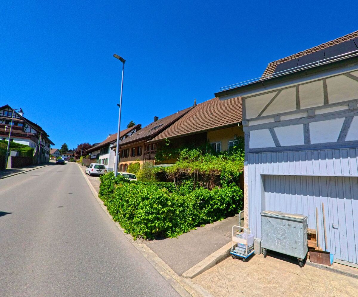 In einer leicht ansteigenden Strasse von Hochfelden im Kanton Zürich (PLZ 8182) reihen sich traditionelle Wohnhäuser mit Vorgärten und Fachwerkfassaden aneinander.