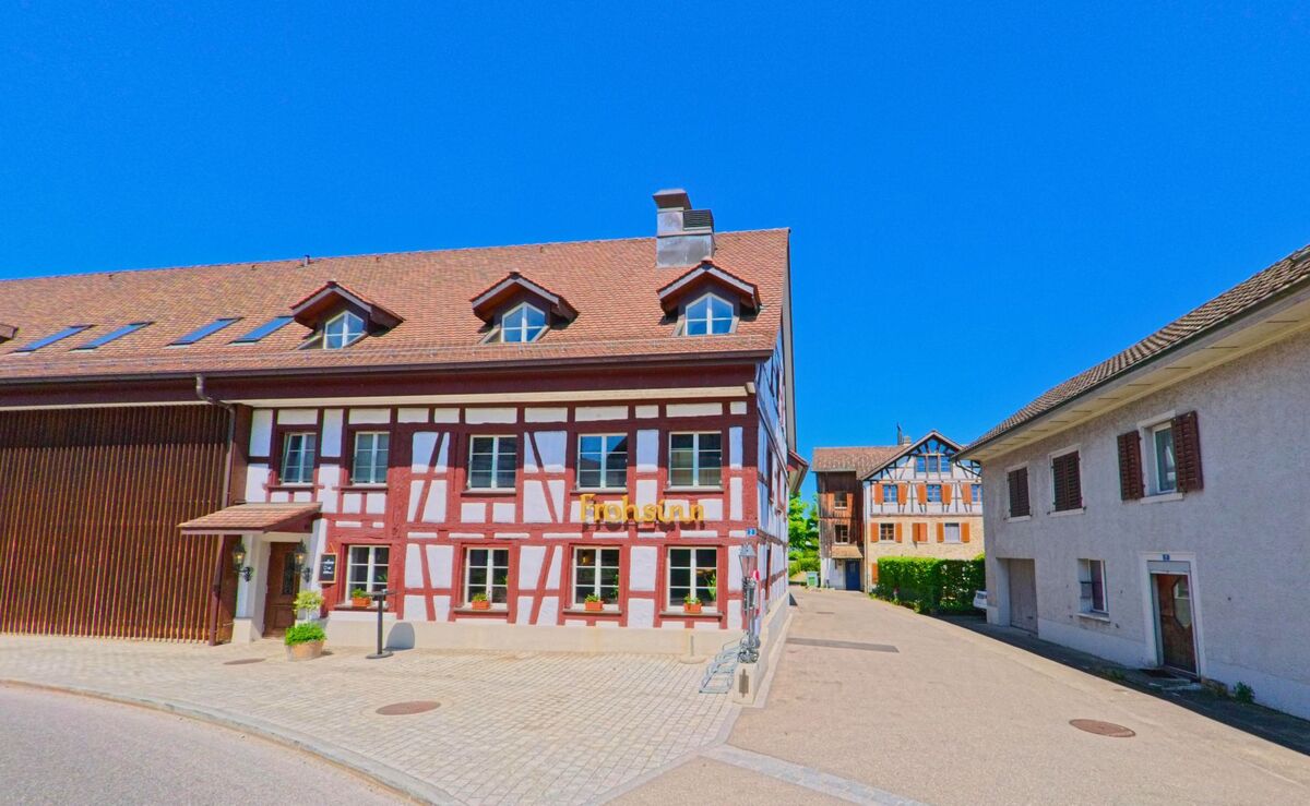 Ein Fachwerkhaus mit der Aufschrift „Frohsinn“ steht im Zentrum von Hochfelden (PLZ 8182) im Kanton Zürich an einer kleinen Seitenstrasse mit Kopfsteinpflaster.