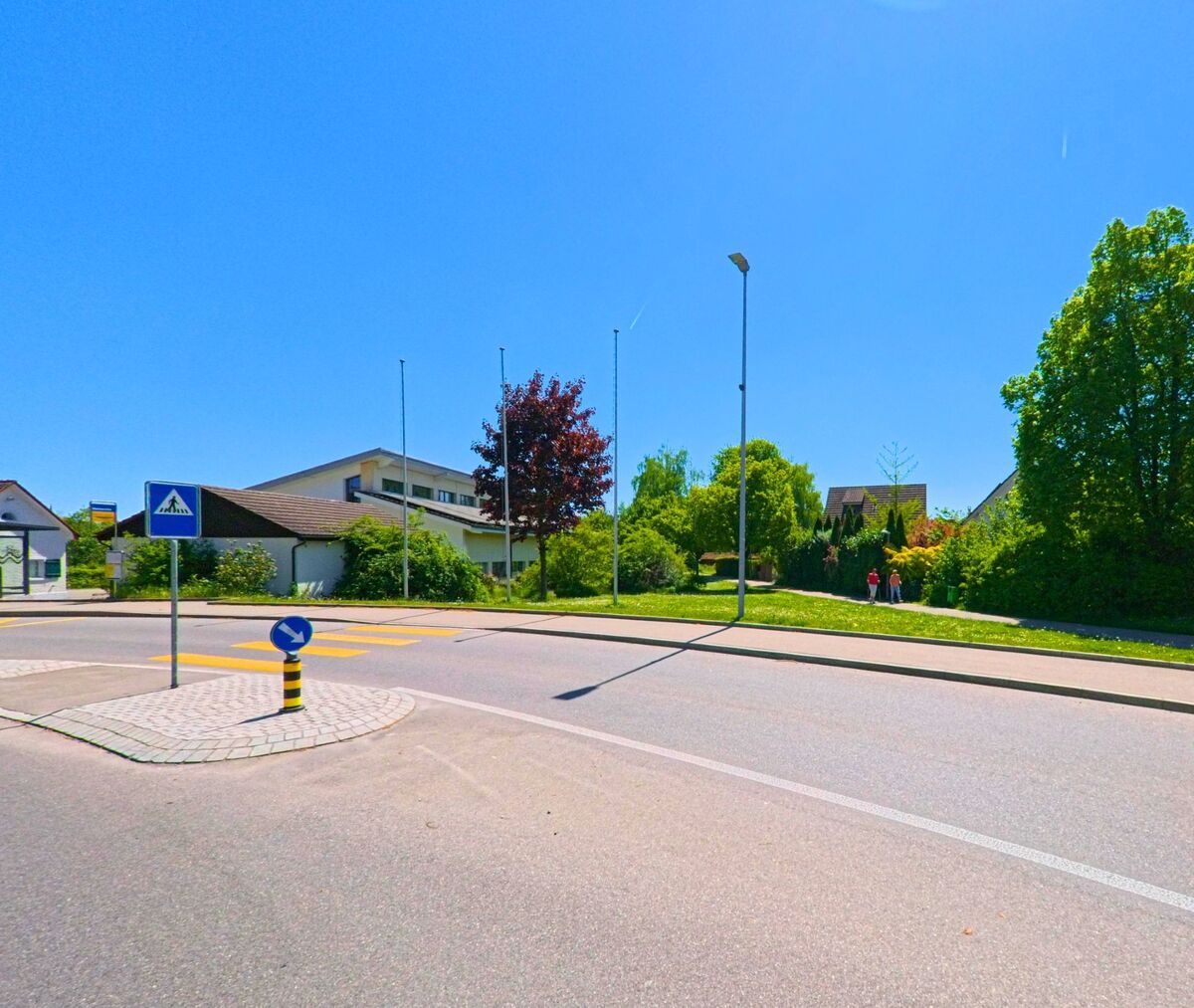 Eine Verkehrsinsel mit Fussgängerstreifen und Hinweisschild befindet sich in Hochfelden (PLZ 8182) im Kanton Zürich an einer ruhigen Quartierstrasse mit viel Grün.